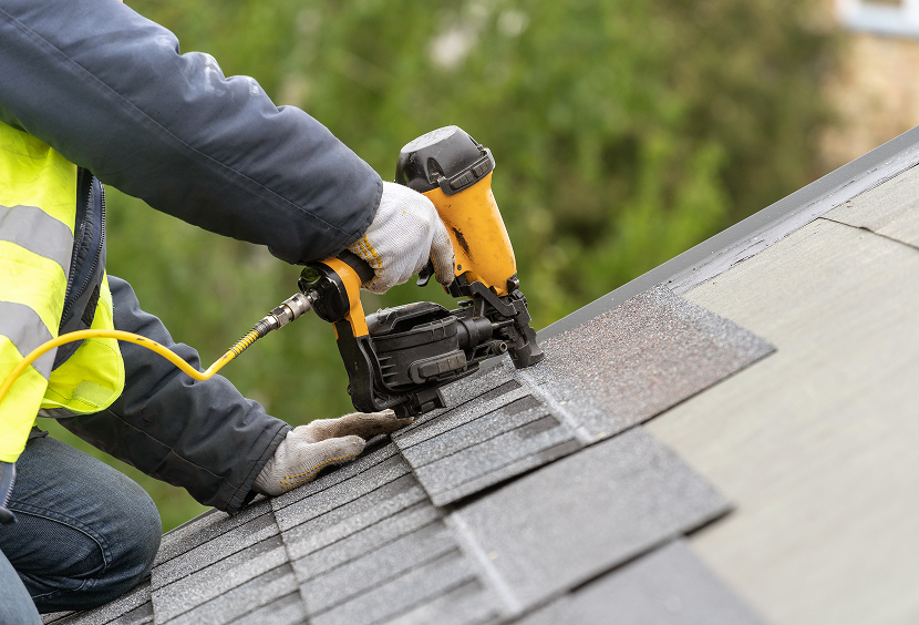 Roofer securing asphalt shingles on roof.